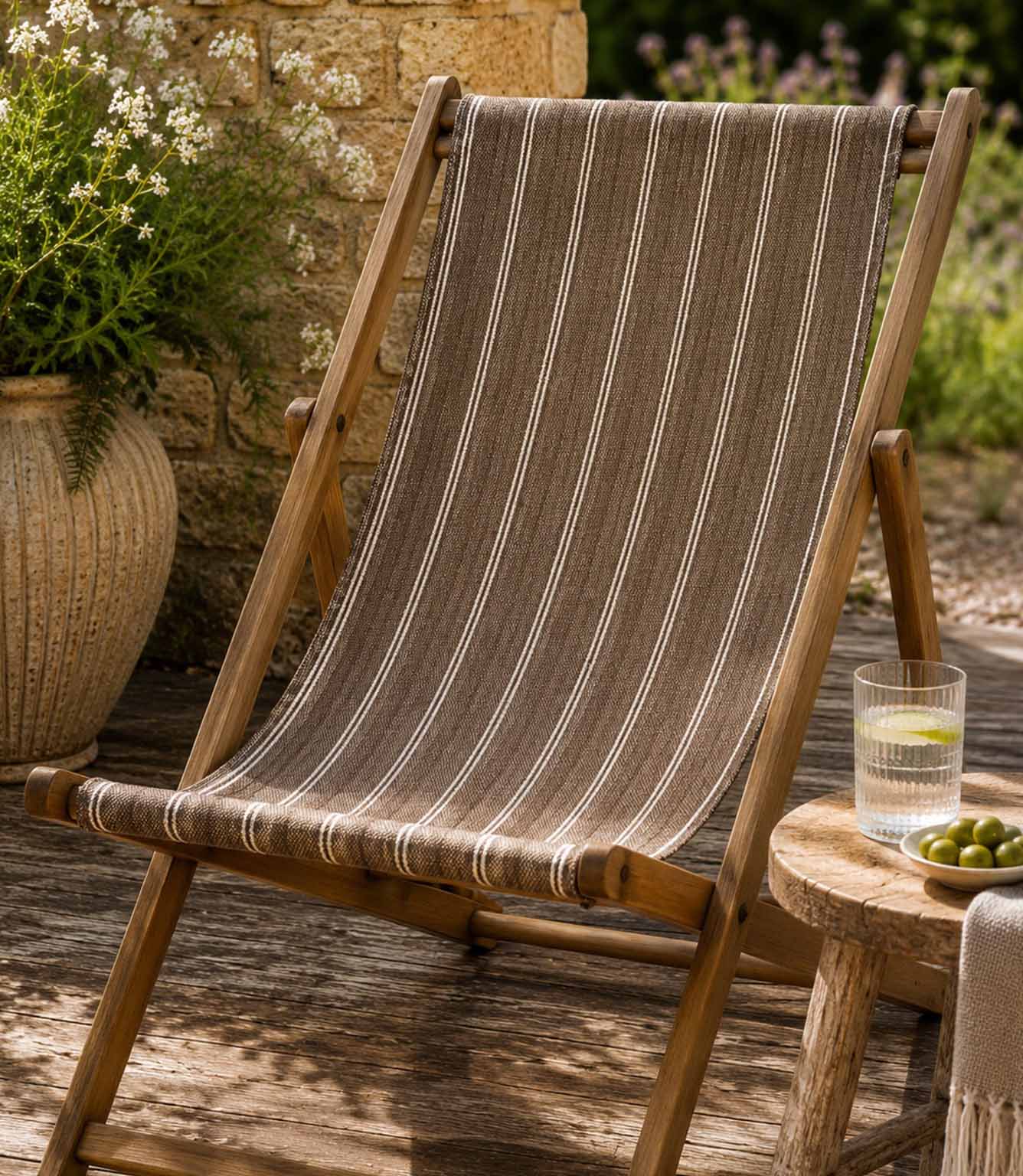 Wooden deck chair with striped brown outdoor fabric on a wooden deck, in a garden setting