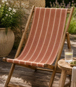 Wooden deck chair with striped orange outdoor fabric on a wooden deck, in a garden setting