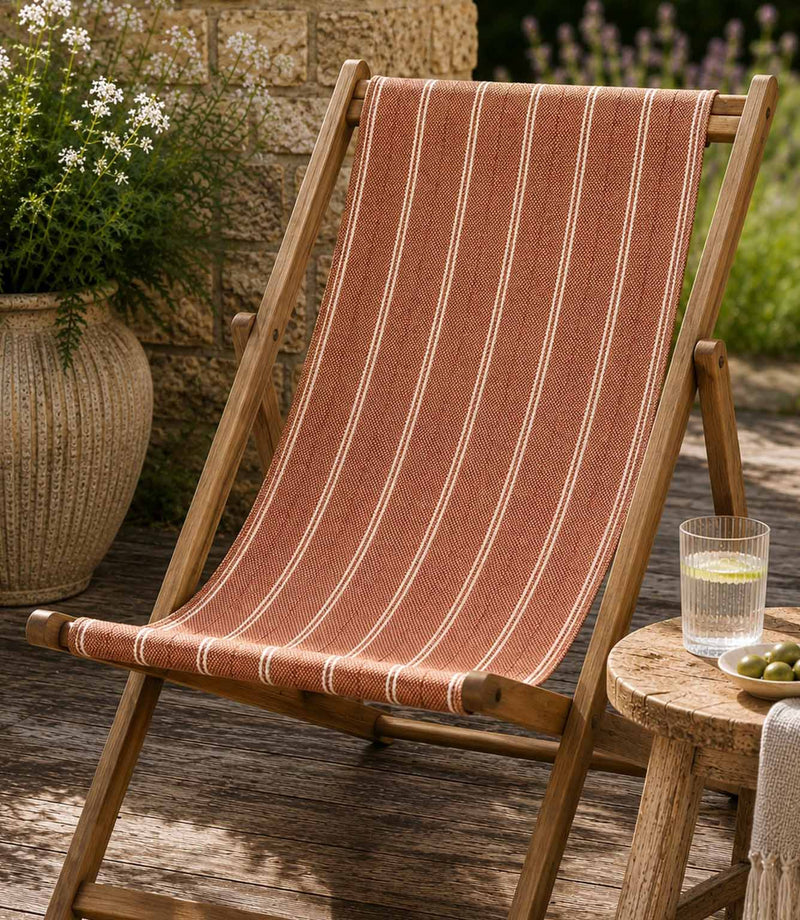 Wooden deck chair with striped orange outdoor fabric on a wooden deck, in a garden setting