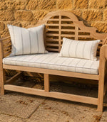 Wooden bench with striped outdoor fabric cushions against a stone wall.