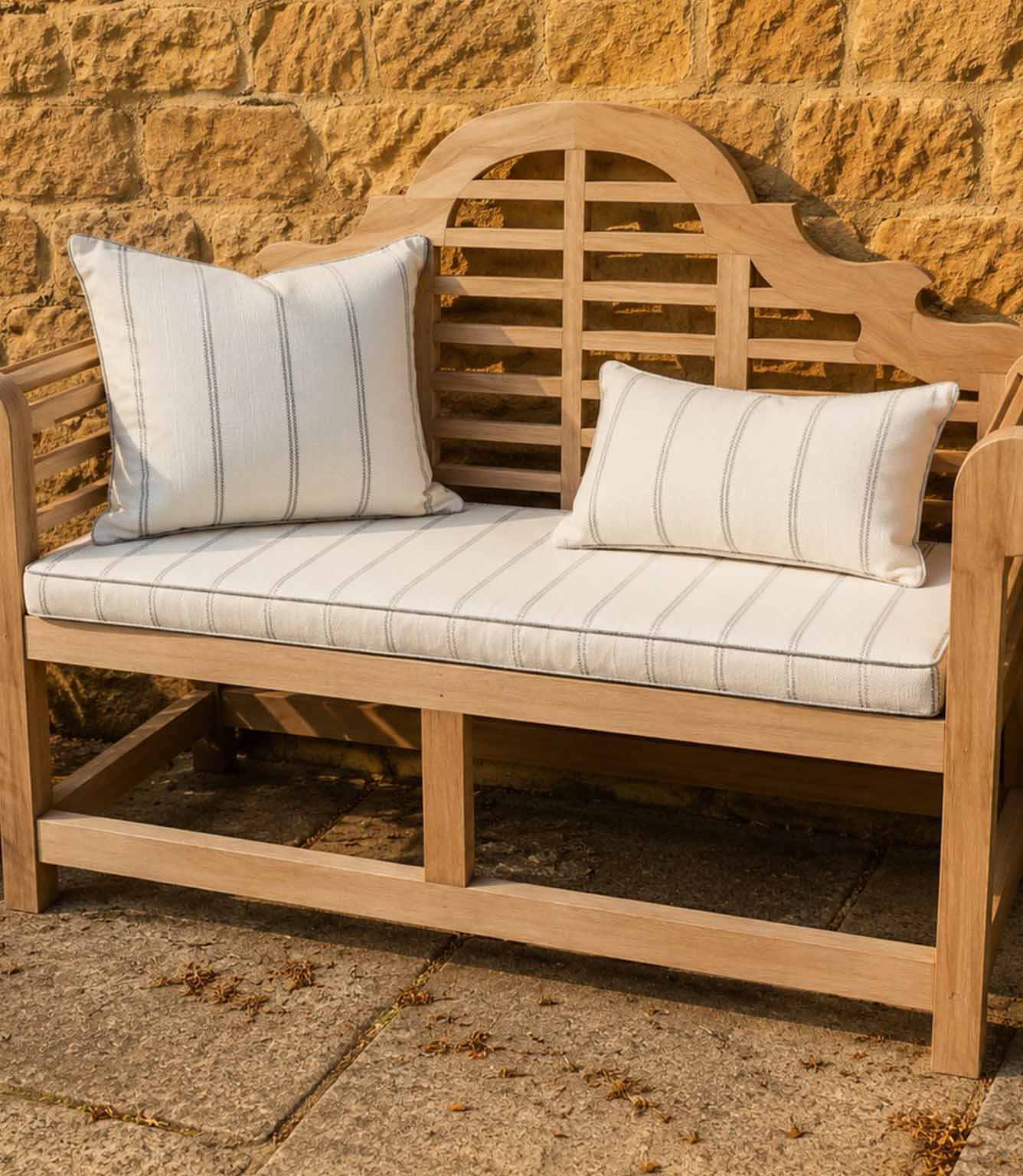 Wooden bench with striped outdoor fabric cushions against a stone wall.