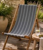 Wooden deck chair with striped blue outdoor fabric on a wooden deck, in a garden setting