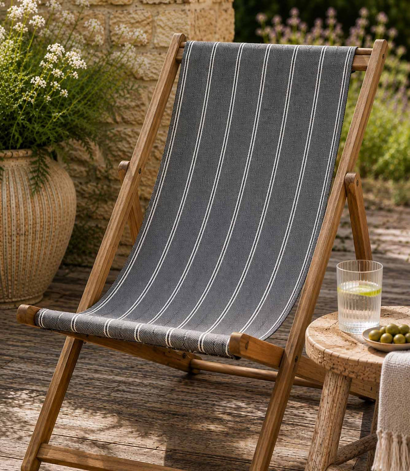 Wooden deck chair with striped blue outdoor fabric on a wooden deck, in a garden setting