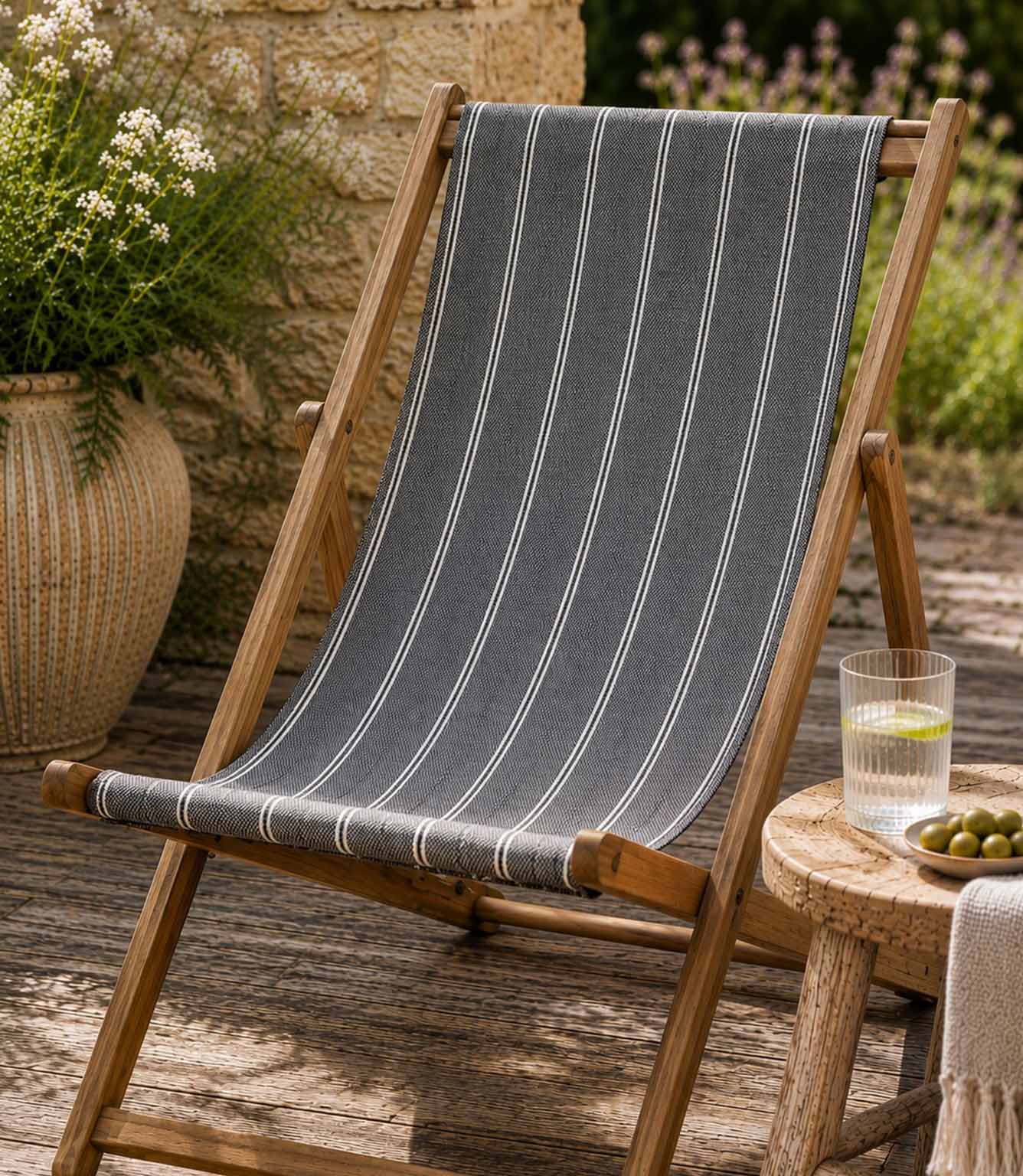 Wooden deck chair with striped blue outdoor fabric on a wooden deck, in a garden setting