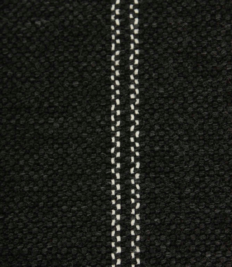 Close-up detail of black textured woven fabric featuring narrow white stitched stripe detailing.