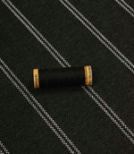 Charcoal striped upholstery fabric shown with a black thread spool, highlighting the scale and woven texture.