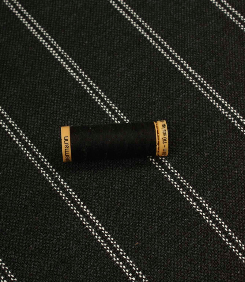 Charcoal striped upholstery fabric shown with a black thread spool, highlighting the scale and woven texture.