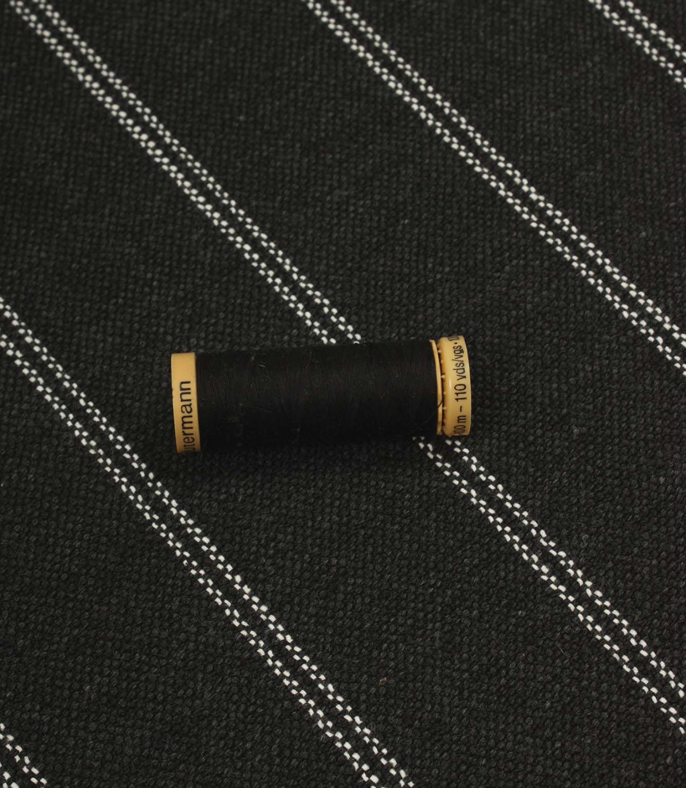 Charcoal striped upholstery fabric shown with a black thread spool, highlighting the scale and woven texture.
