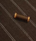 Brown striped upholstery fabric displayed with a matching brown thread spool to show scale and texture.