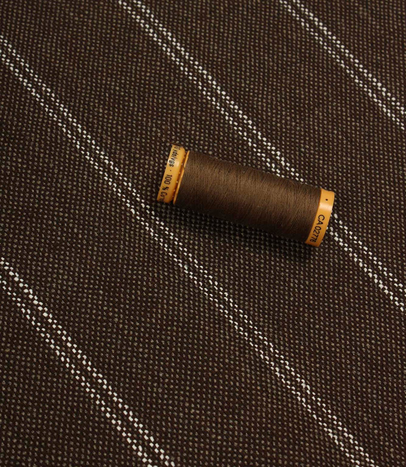 Brown striped upholstery fabric displayed with a matching brown thread spool to show scale and texture.