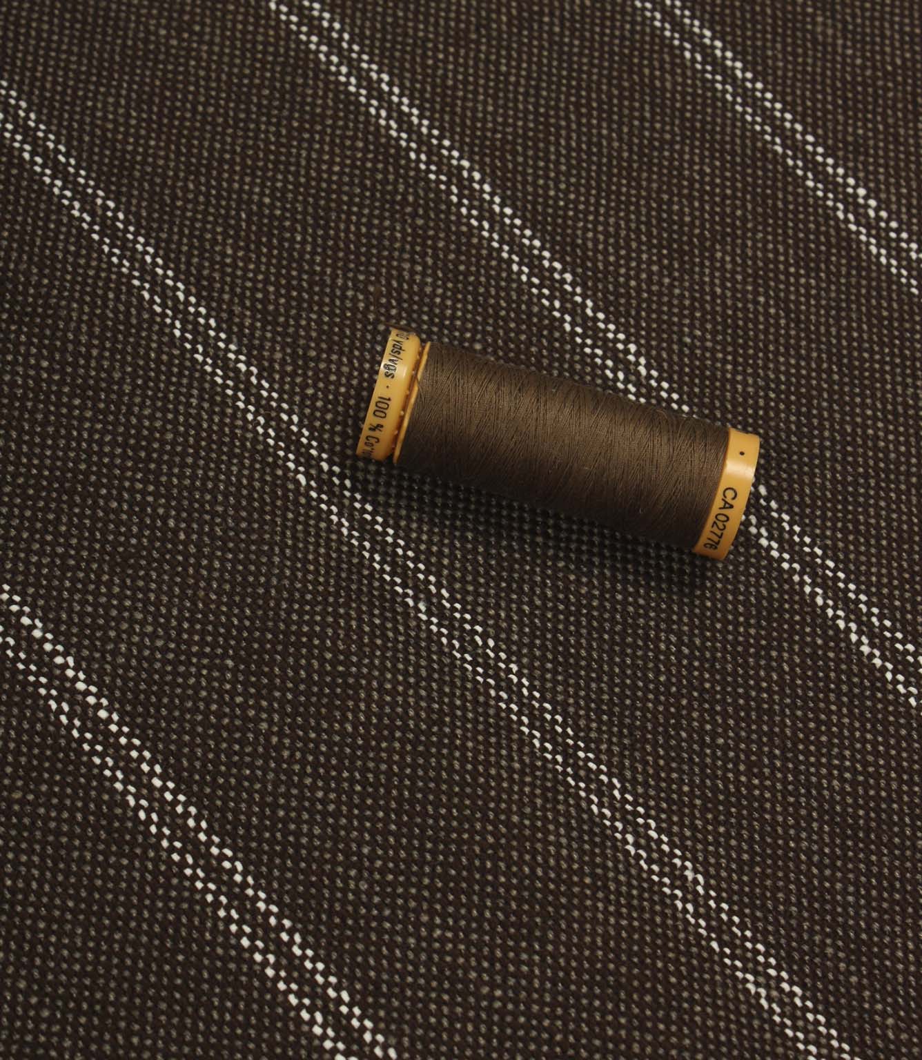 Brown striped upholstery fabric displayed with a matching brown thread spool to show scale and texture.
