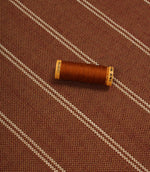Copper striped upholstery fabric displayed with a matching thread spool to highlight scale and woven texture.