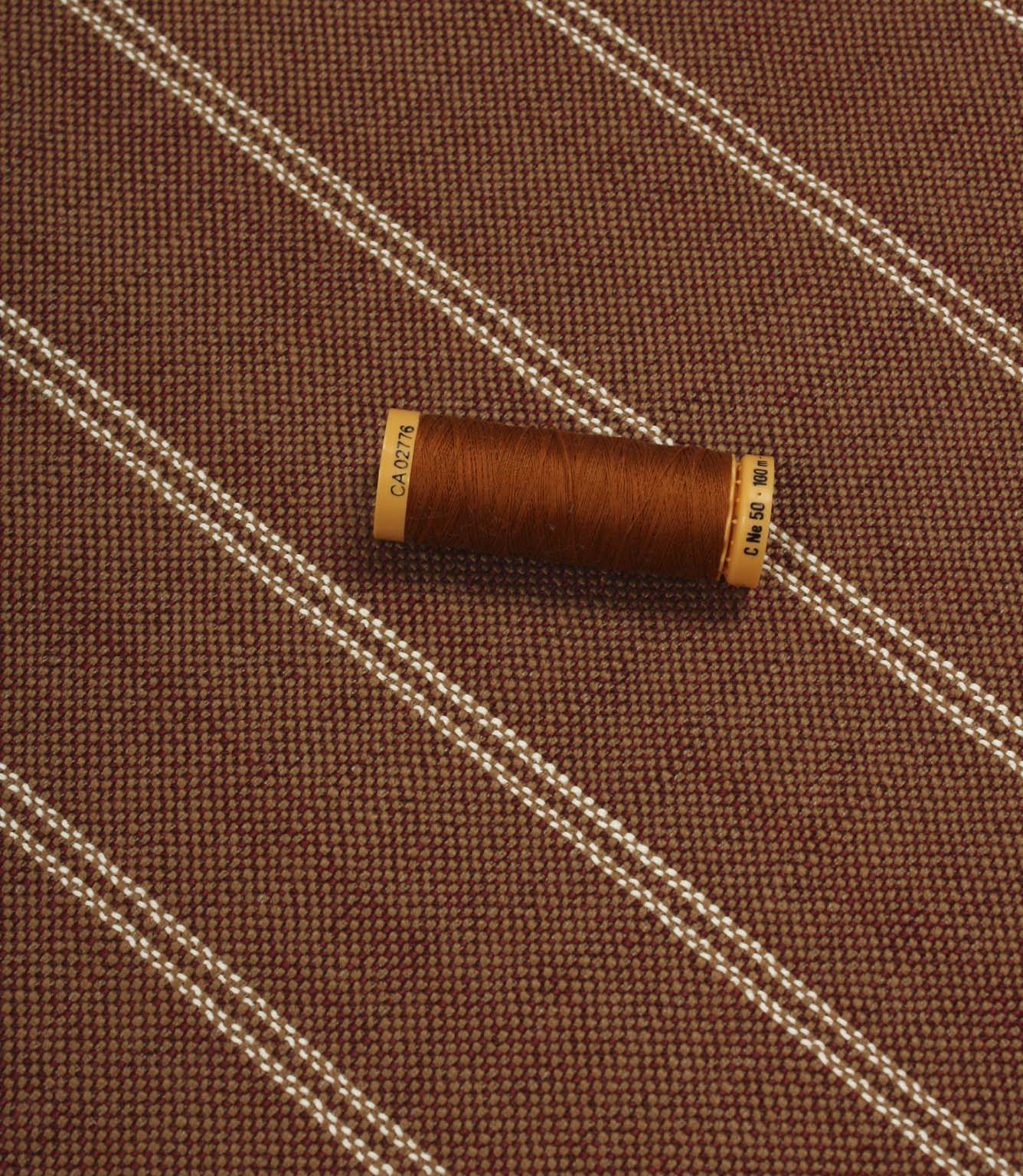 Copper striped upholstery fabric displayed with a matching thread spool to highlight scale and woven texture.