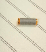 Ecru striped upholstery fabric displayed with a grey thread spool to highlight scale and woven texture.