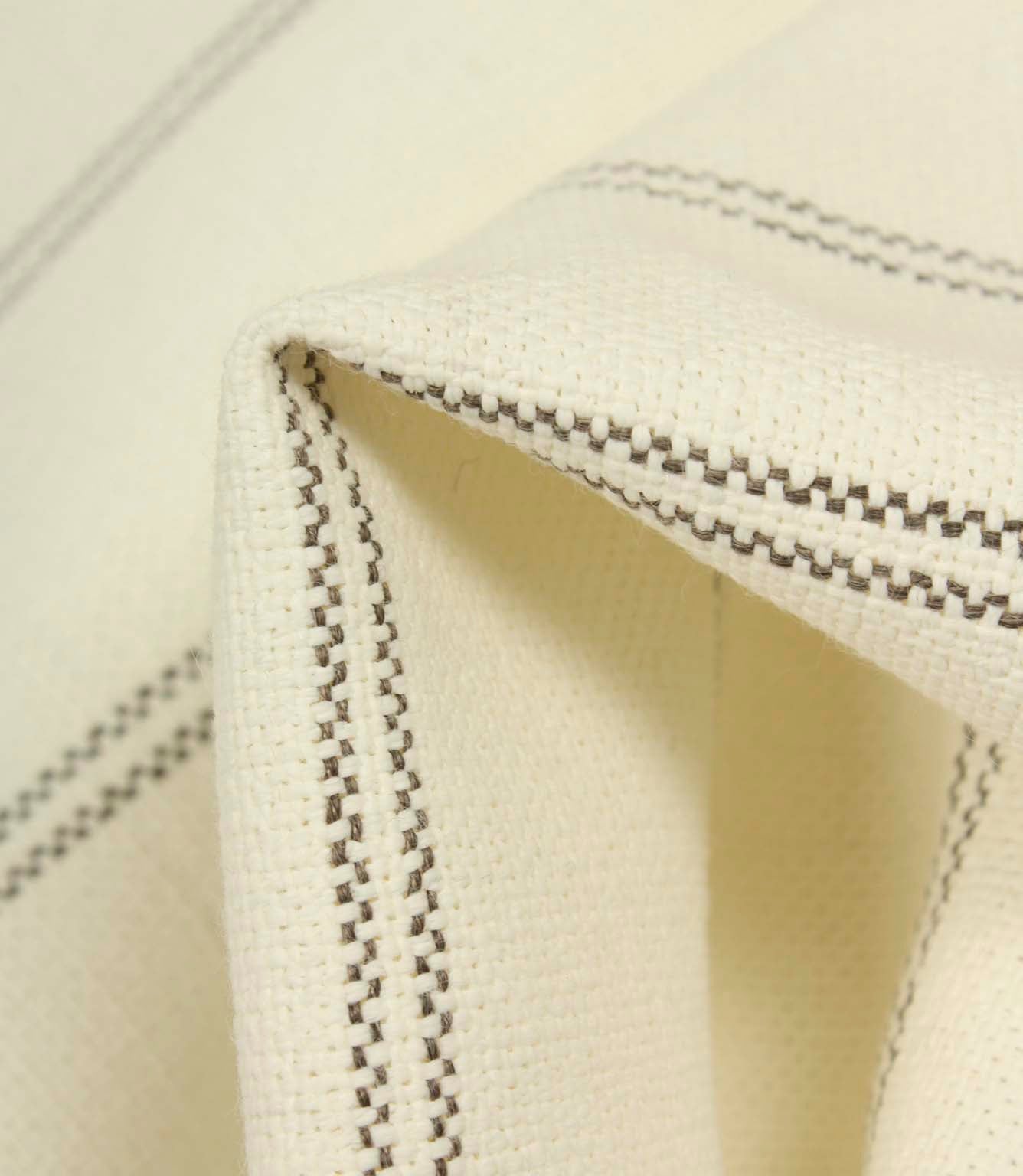 Macro detail of ecru upholstery fabric showing the textured weave and delicate grey stitched stripes.