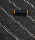Ink blue striped upholstery fabric displayed with a matching dark thread spool to highlight scale and woven texture.