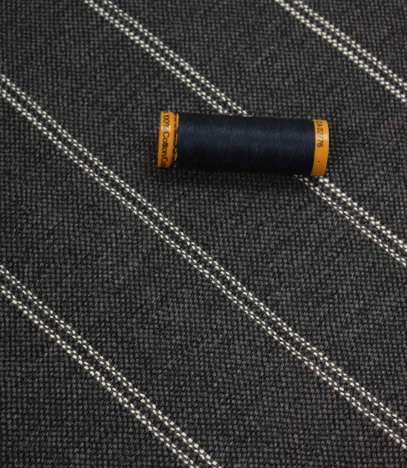 Ink blue striped upholstery fabric displayed with a matching dark thread spool to highlight scale and woven texture.