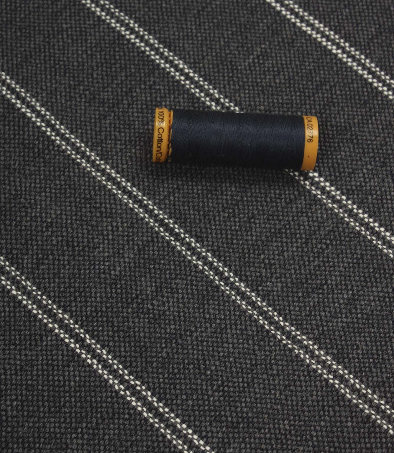 Ink blue striped upholstery fabric displayed with a matching dark thread spool to highlight scale and woven texture.