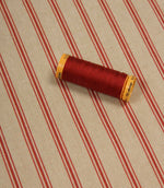 Red striped furnishing fabric styled with matching red thread spool to highlight colour coordination and texture.