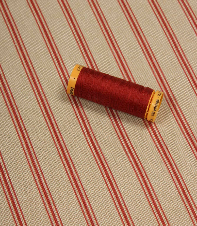 Red striped furnishing fabric styled with matching red thread spool to highlight colour coordination and texture.