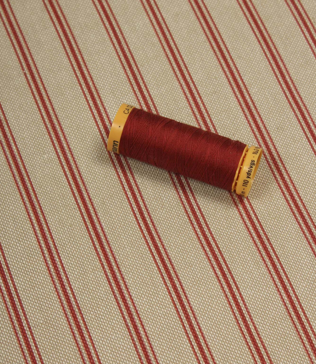 Red striped furnishing fabric styled with matching red thread spool to highlight colour coordination and texture.