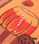 Close-up of the Pumpkin Spice velvet cushion showing the orange and red embroidered pumpkin-shaped drink, striped straw and jack-o'-lantern details on soft velvet.