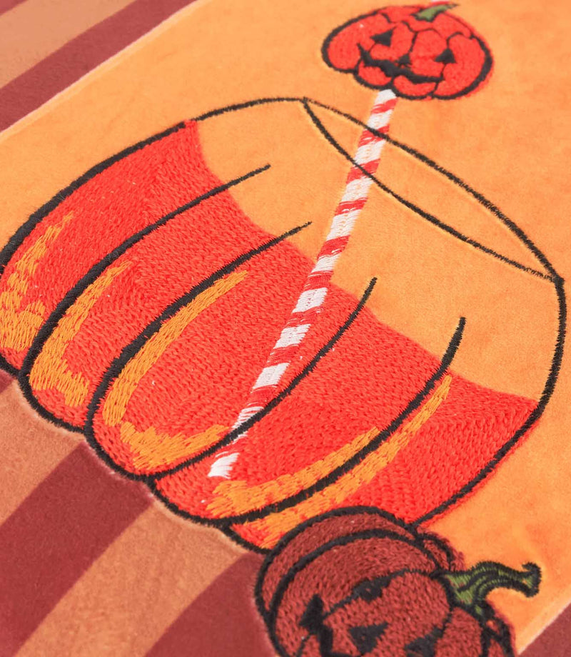Close-up of the Pumpkin Spice velvet cushion showing the orange and red embroidered pumpkin-shaped drink, striped straw and jack-o'-lantern details on soft velvet.