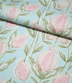 Rithani Robin's Egg botanical fabric partially folded, displaying its repeating pink and cream pomegranate pattern with delicate green foliage on a soft duck egg blue woven background.
