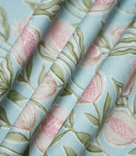 Rithani Robin's Egg fabric gathered into soft, flowing folds, showing its natural drape and repeating botanical design of pink pomegranates and sage green foliage against a duck egg blue background.