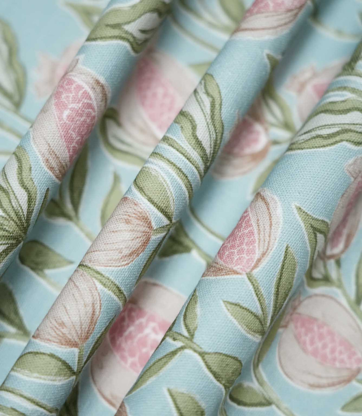 Rithani Robin's Egg fabric gathered into soft, flowing folds, showing its natural drape and repeating botanical design of pink pomegranates and sage green foliage against a duck egg blue background.