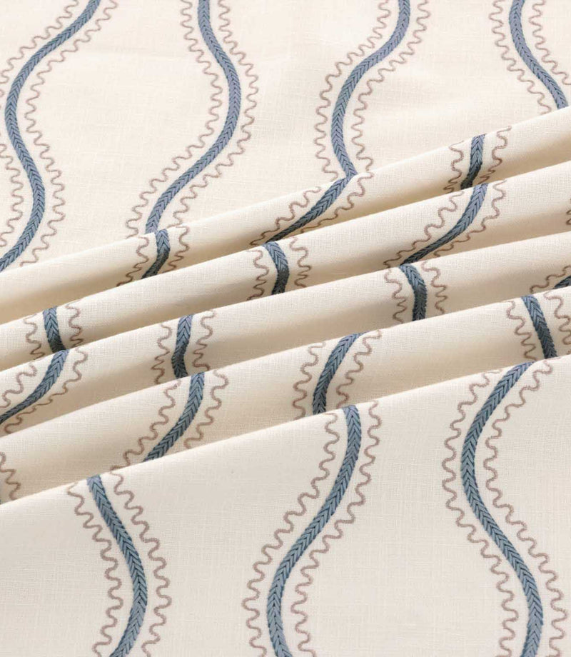 Riverhead Nautica fabric arranged in soft folds, highlighting the raised blue embroidered wavy stripes, taupe scalloped detailing and ivory woven texture.