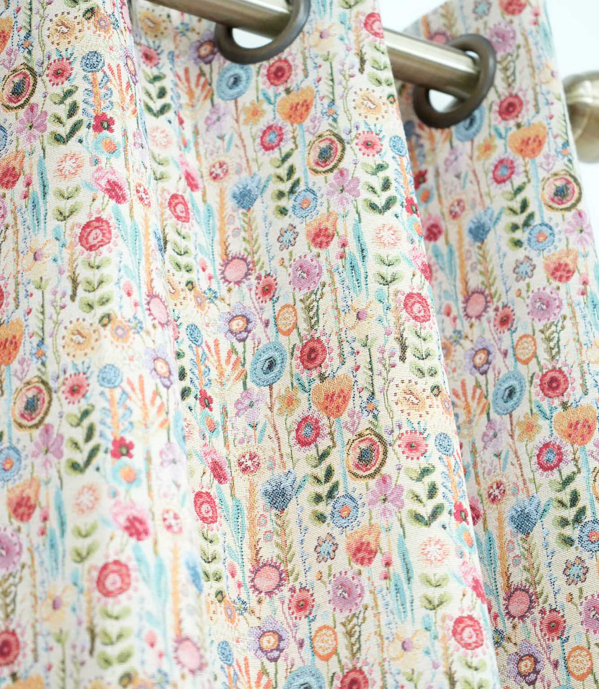 Rosalia Multi floral curtain fabric featuring a colourful wildflower design in pink, blue, orange, purple and green on a natural cream background, styled as eyelet curtains.