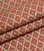 Folded patterned fabric showing the detailed woven texture and repeating geometric motif in rust red, cream, and taupe tones.