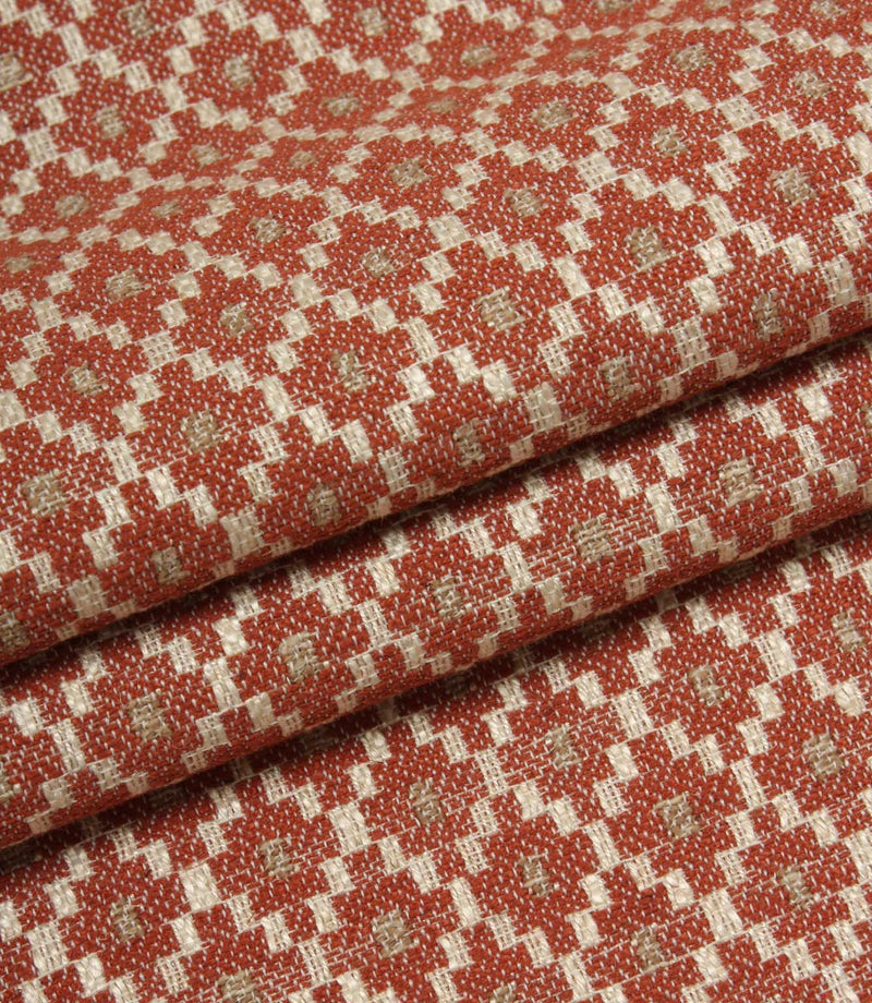 Folded patterned fabric showing the detailed woven texture and repeating geometric motif in rust red, cream, and taupe tones.