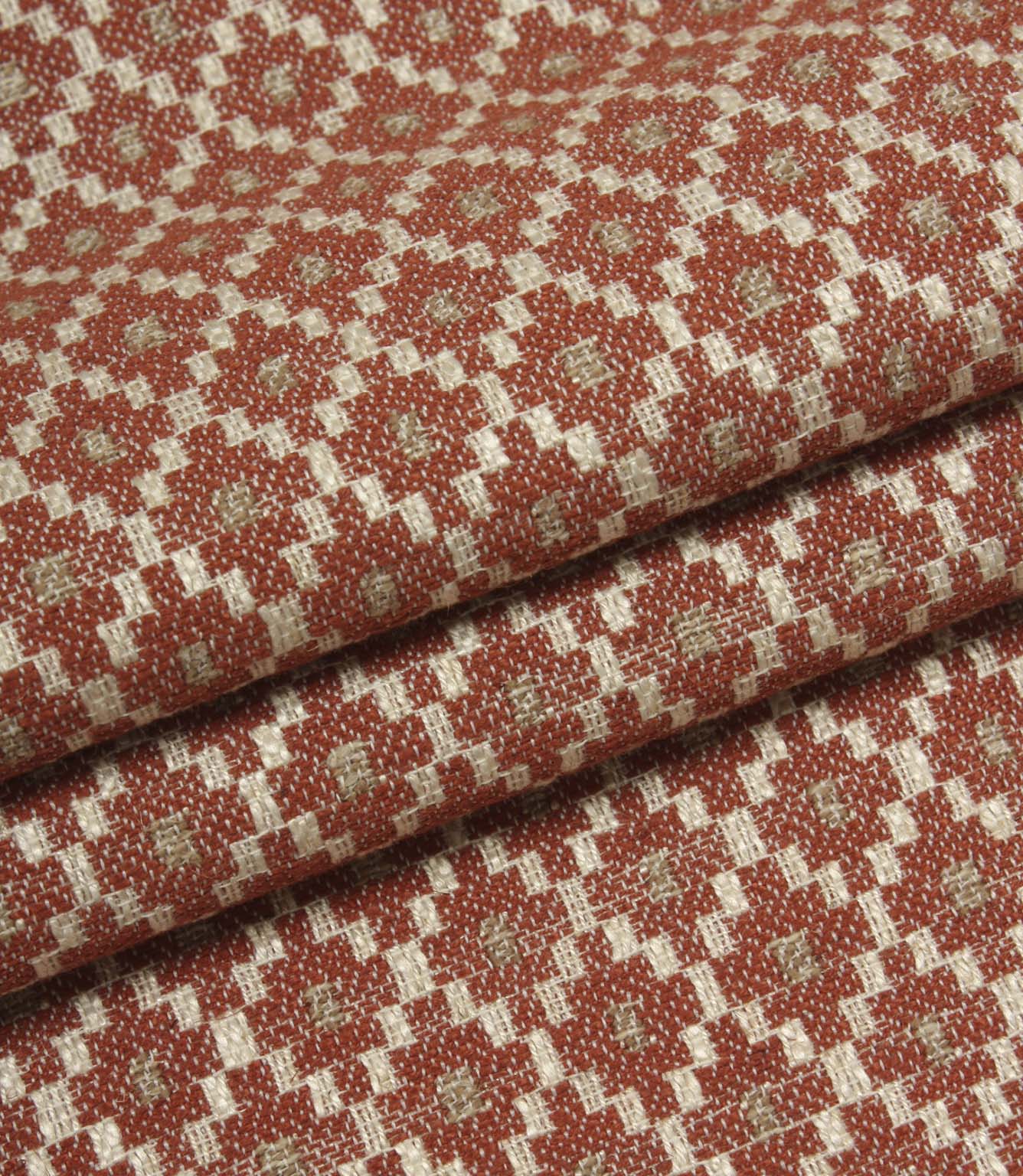 Folded patterned fabric showing the detailed woven texture and repeating geometric motif in rust red, cream, and taupe tones.