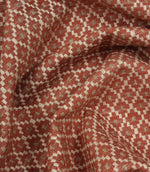 Draped geometric upholstery fabric with a soft woven handle and intricate rust red and cream lattice-inspired pattern.