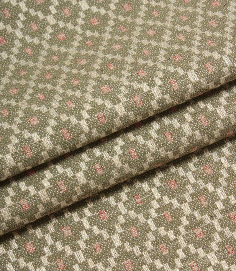 Folded patterned fabric showing the detailed woven texture and repeating geometric motif in sage green, cream, and blush pink tones.