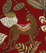 Close-up of woven leopard motif on rich red decorative fabric with textured botanical accents.