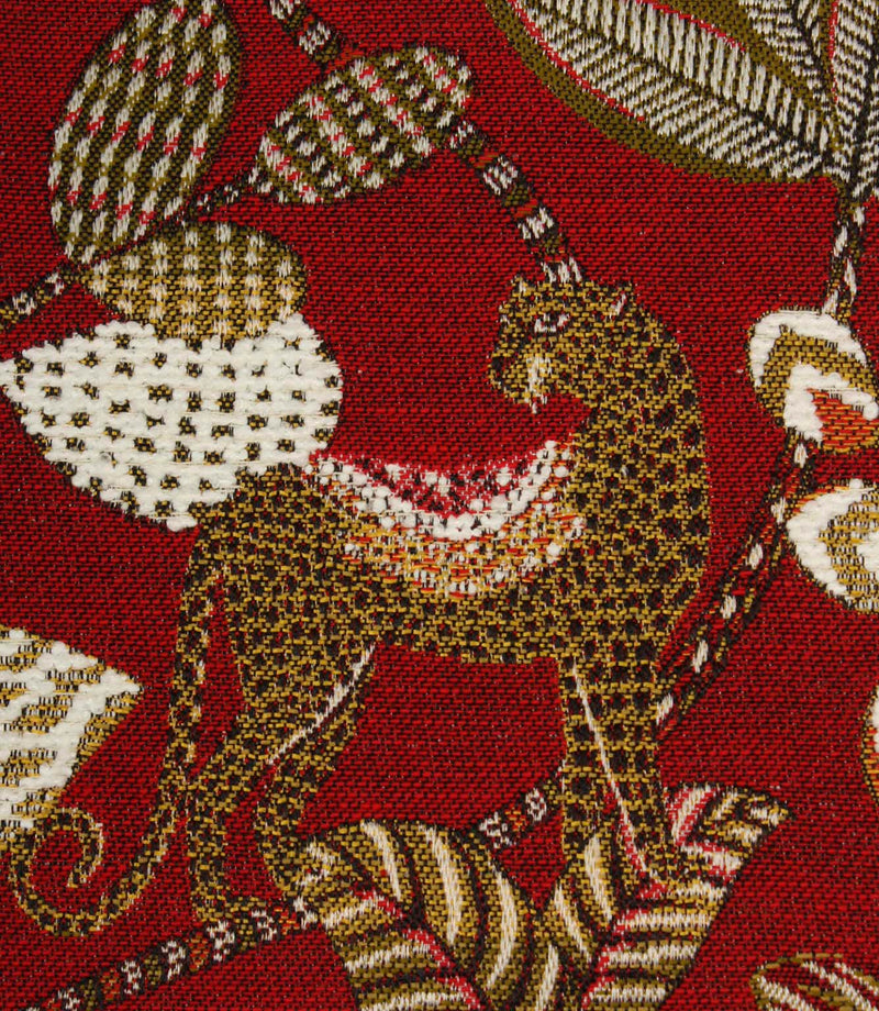 Close-up of woven leopard motif on rich red decorative fabric with textured botanical accents.