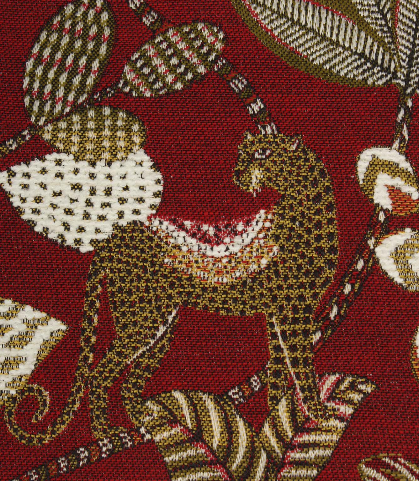 Close-up of woven leopard motif on rich red decorative fabric with textured botanical accents.
