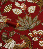 Red animal print upholstery fabric with large leaf motifs and coordinating thread reel for colour reference.