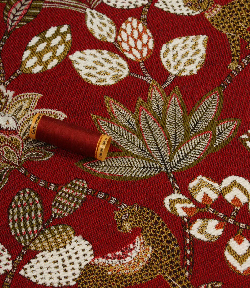 Red animal print upholstery fabric with large leaf motifs and coordinating thread reel for colour reference.