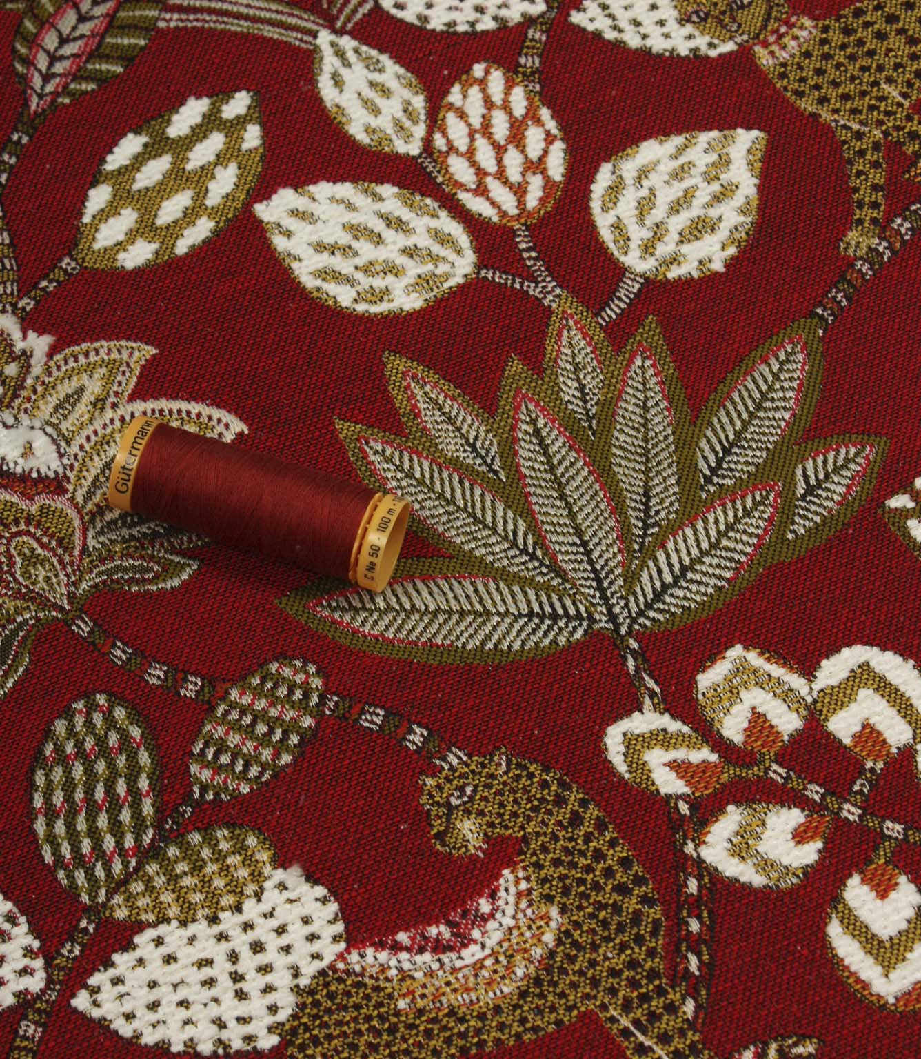 Red animal print upholstery fabric with large leaf motifs and coordinating thread reel for colour reference.
