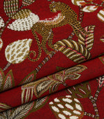 Folded red woven fabric featuring exotic leopards, floral detailing and bold botanical shapes.
