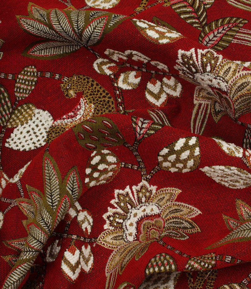 Draped red jacquard fabric with decorative jungle-inspired animal and floral pattern.