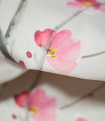 Macro photograph of Seville Blossom Stone fabric highlighting the fine woven texture and watercolour floral detailing, with soft pink petals, raspberry shading, small yellow stamens and grey-green branches.
