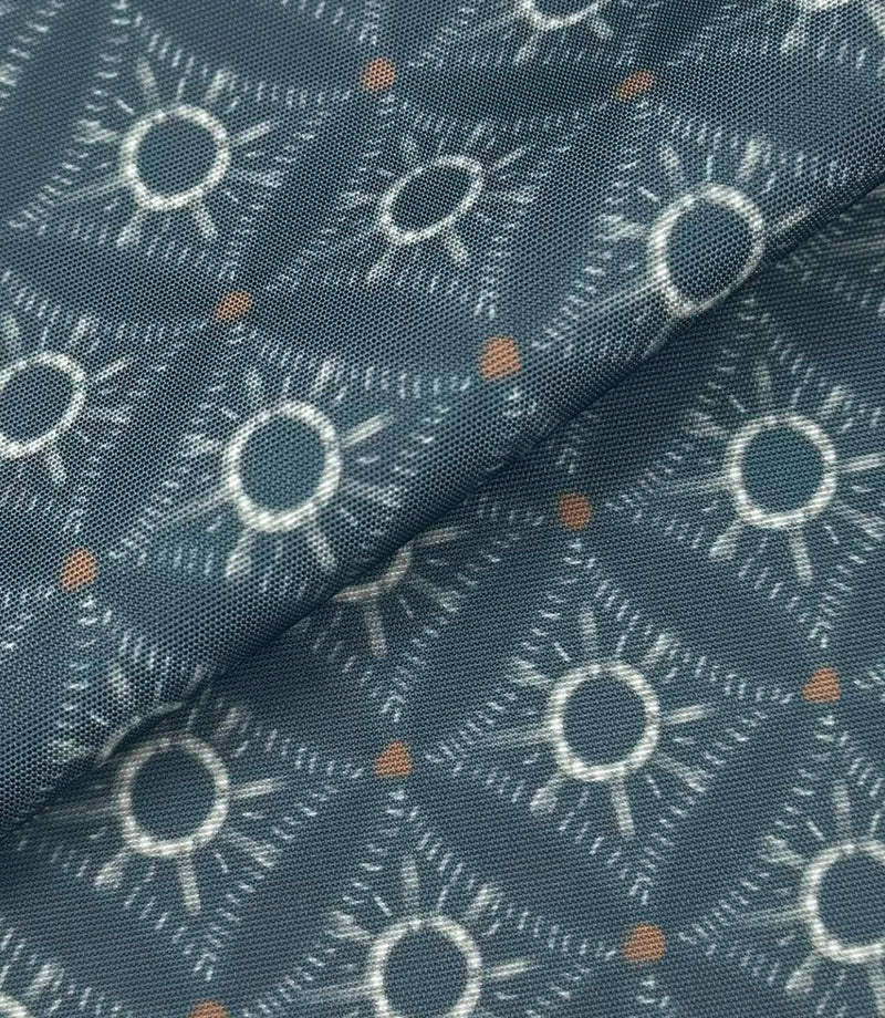 Folded Solstice Halo outdoor fabric featuring ivory geometric sunburst motifs on a muted blue background with small rust accents.