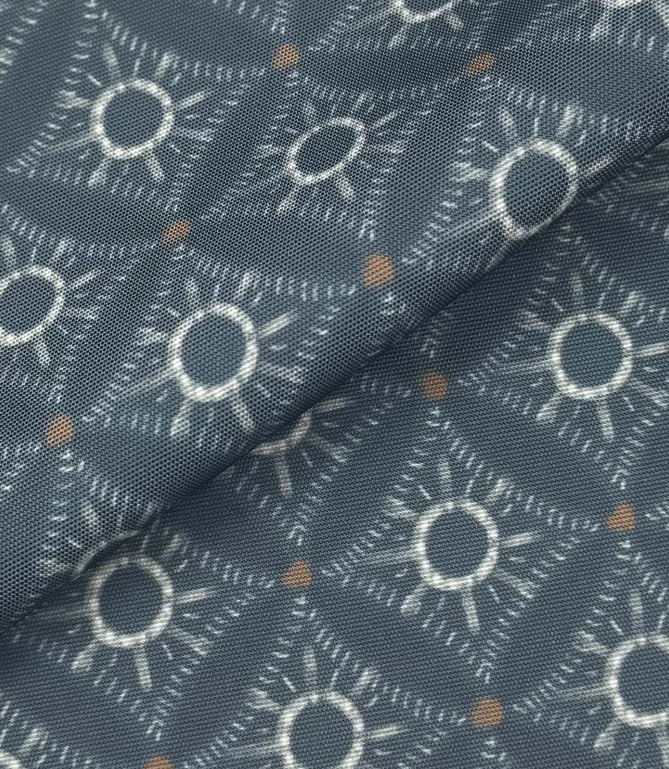 Folded Solstice Halo outdoor fabric featuring ivory geometric sunburst motifs on a muted blue background with small rust accents.