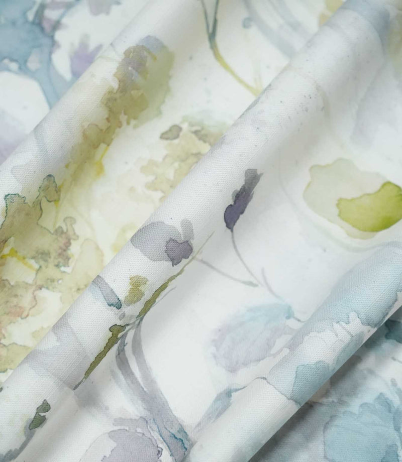 Sorong Lemon floral fabric gathered into flowing folds, displaying its natural drape and airy botanical pattern of pale blue and lavender wildflowers with soft yellow and sage green foliage.