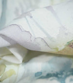 Macro photograph of Sorong Lemon fabric showing its fine woven texture and delicate watercolour print, with softly blended lavender, pale blue and muted yellow-green botanical details on an off-white ground.